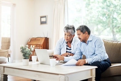 Older Couple Sitting on Couch Looking at Laptop